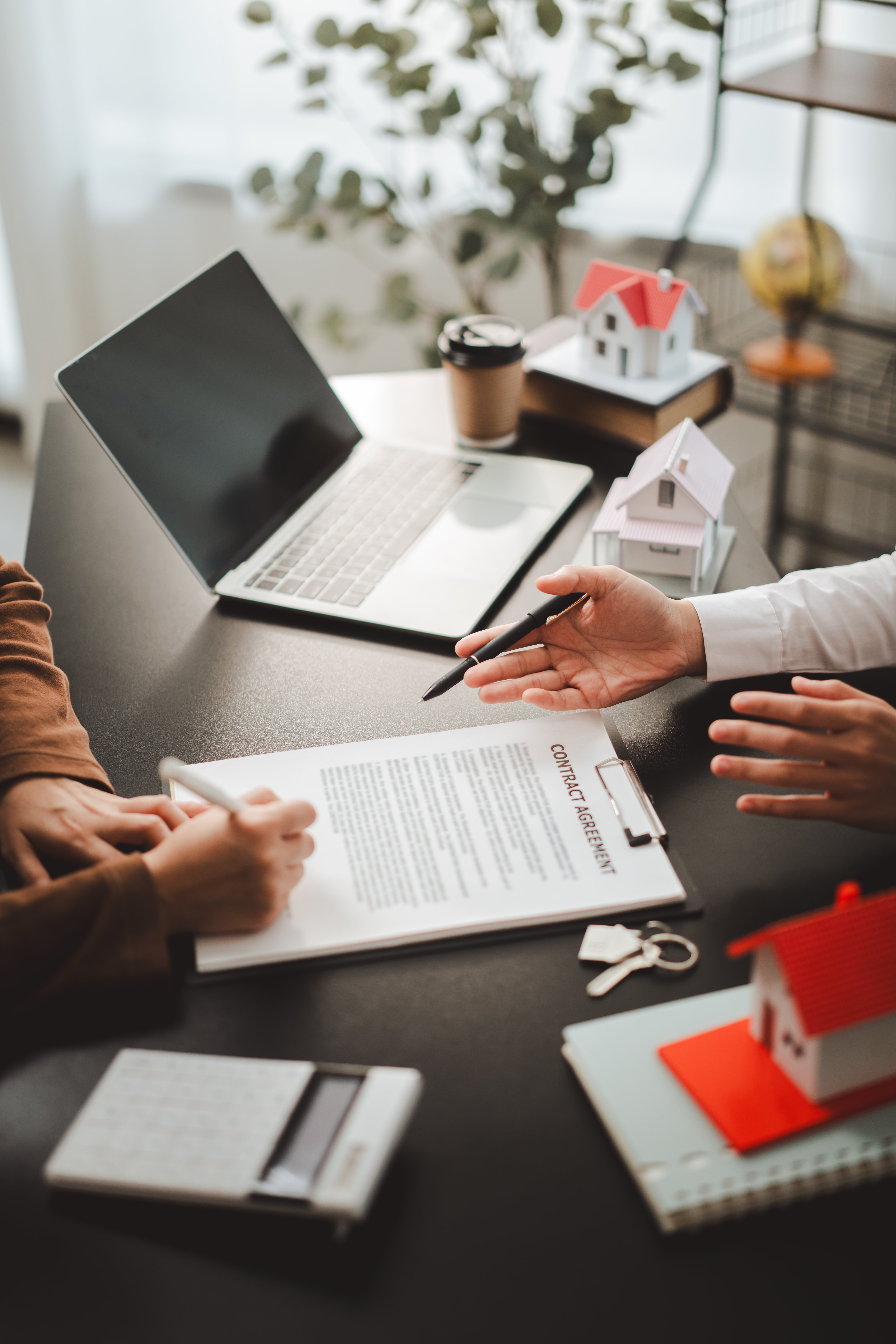 Two people are signing a contract agreement for a new real estate purchase, with one person's hand holding a pen over the document and an agent pointing to details, signifying a property transaction